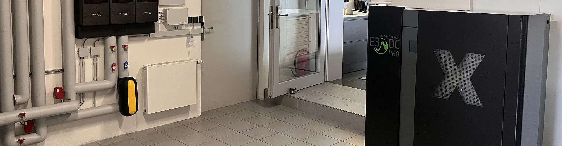 Ein Technikraum zeigt verschiedene Heizungs- und Energiespeichersysteme, darunter eine E3/DC PRO Anlage mit großem X-Symbol.