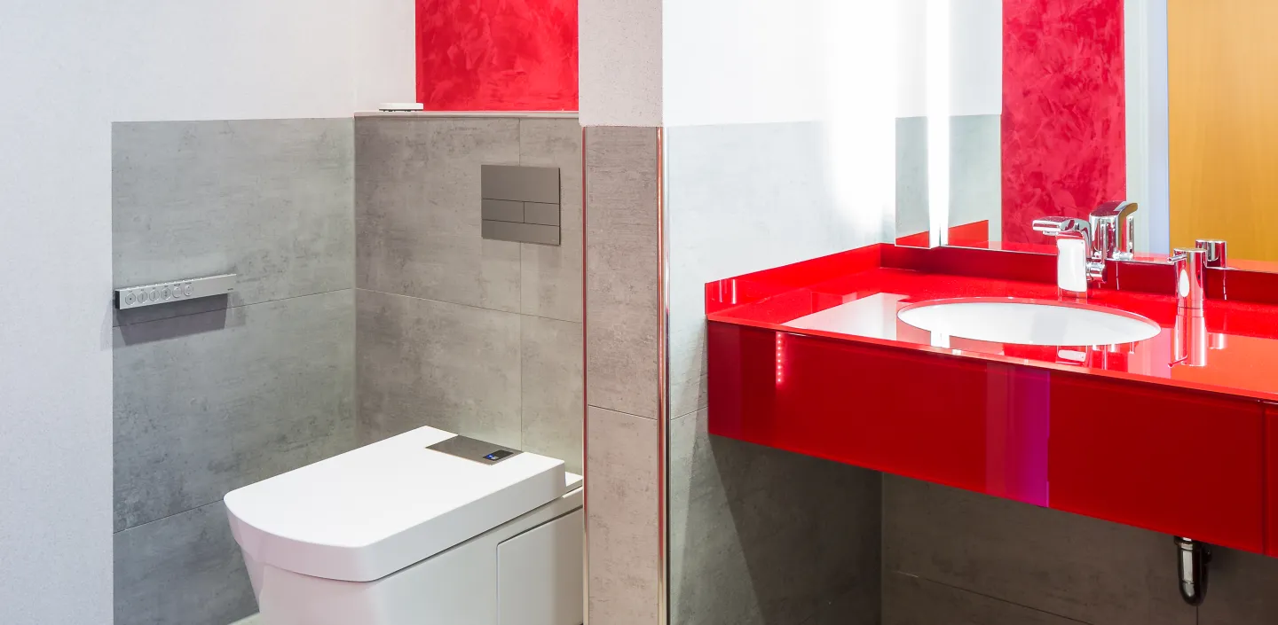 Ein modernes Badezimmer mit einem weißen, wandhängenden WC und einer leuchtend roten Waschtischoberfläche, die mit einem eingebauten Waschbecken ausgestattet ist.