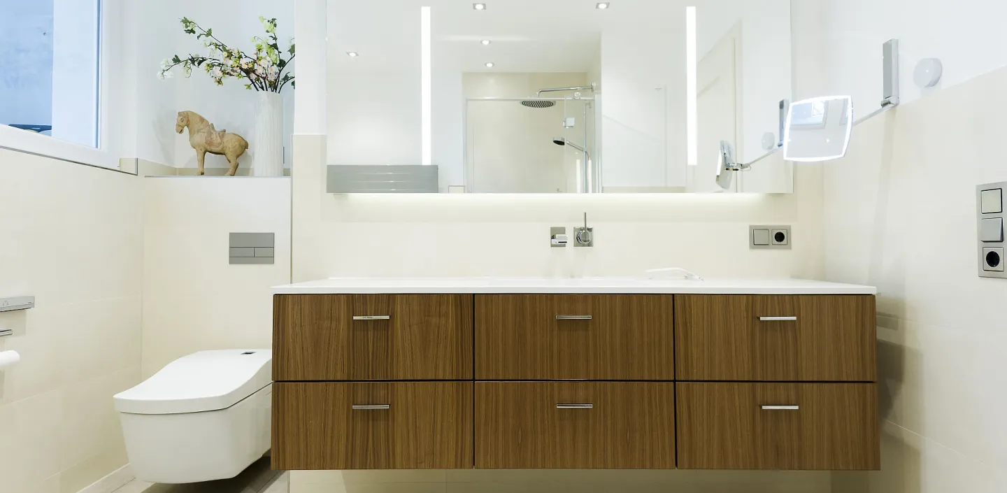 Badezimmer mit modernem Waschtisch aus Holz, LED-Spiegel und hellen Fliesen. 