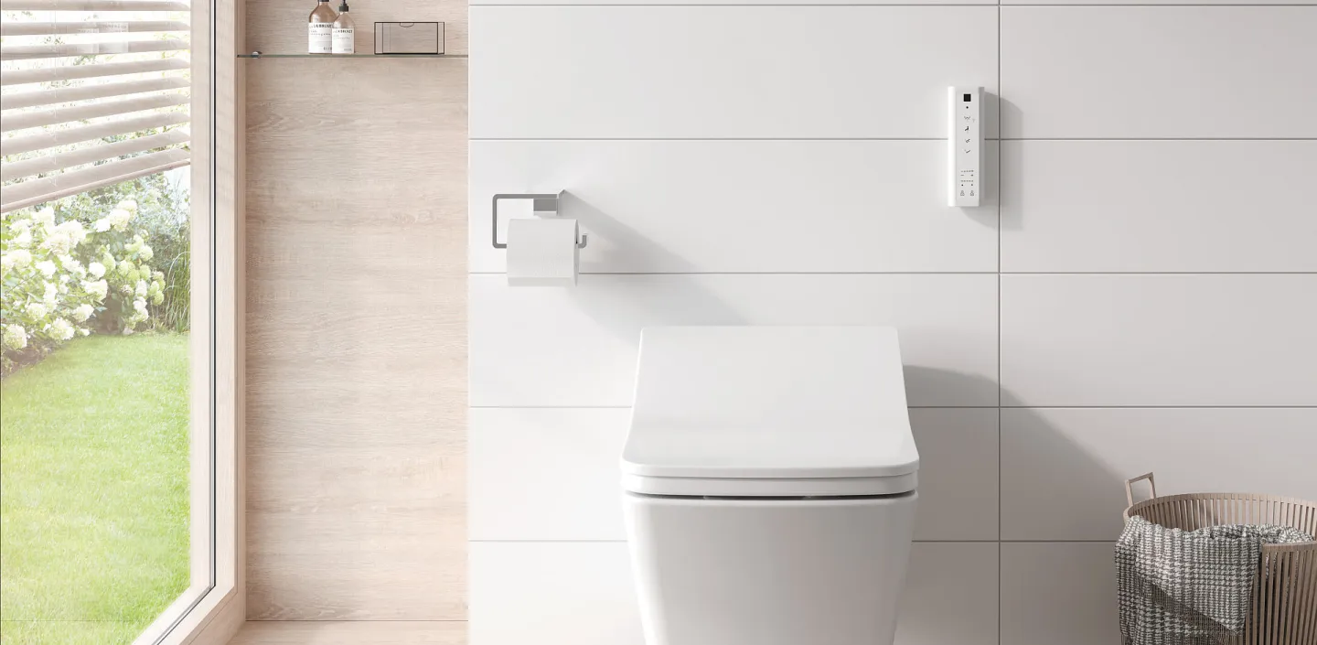 Ein wandhängendes, vor weißen Fliesen montiertes Toto WASHLET SX mit kompakter, abgerundeter Form und leicht geneigtem Deckel. 