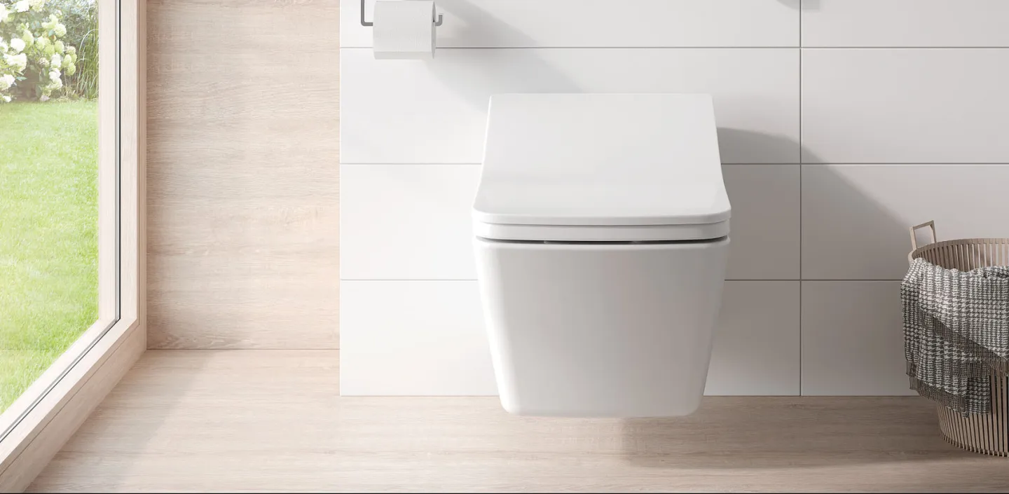 Ein wandhängendes, vor weißen Fliesen montiertes Toto WASHLET SX mit kompakter, abgerundeter Form und leicht geneigtem Deckel. 