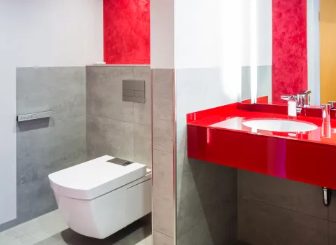 Ein modernes Badezimmer mit einem weißen, wandhängenden WC und einer leuchtend roten Waschtischoberfläche, die mit einem eingebauten Waschbecken ausgestattet ist.