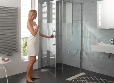 Frau in Handtuch öffnet die Duschtür der AtelierPlan Duschkabine von HSK. 