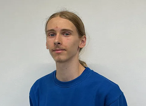 Azubi Filbor Leonhardt in blauer Jacke vor neutralem Hintergrund.