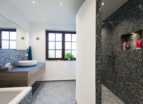 Großes Badezimmer mit blauen Mosaikfliesen, Holzwaschtisch, Glasdusche und großem Fenster.