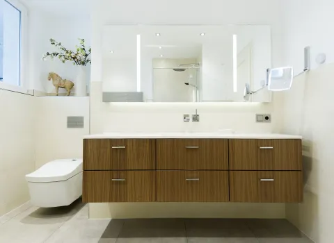 Badezimmer mit modernem Waschtisch aus Holz, LED-Spiegel und hellen Fliesen. 