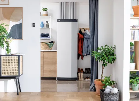 In einem hellen, modern eingerichteten Flur steht eine kompakte Wärmepumpe dezent zwischen Holzregalen und einer offenen Garderobe.