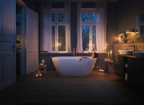 Modernes Badezimmer mit Badewanne, Kerzen und stimmungsvoller Abendbeleuchtung.