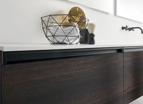 Detailansicht eines Stocco Badmöbels mit dunkler Holzfront, weißer Waschtischplatte und schwarzen Griffleisten.