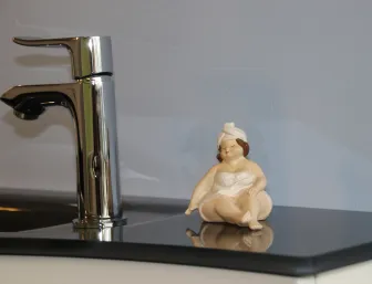 Ein eleganter Chrom-Wasserhahn auf einer glänzenden, schwarzen Oberfläche, daneben eine kleine Keramikfigur, die eine Frau in einem Handtuch darstellt.