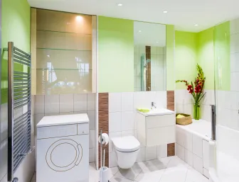 Ein modernes Badezimmer in frischen Grüntönen mit einem wandhängenden WC, einer Waschmaschine und einer Dusch-Badewanne-Kombination. 