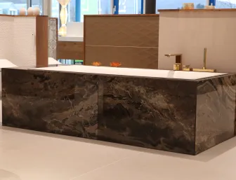 Eine luxuriöse Badewanne mit einer Verkleidung aus glänzendem, braunem Marmor, die in einem modernen Badezimmer-Showroom ausgestellt ist. 