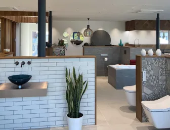 Ein großzügiger Ausstellungsraum für Badezimmer zeigt verschiedene moderne Einrichtungen, darunter freistehende Waschbecken, Toiletten und Badewannen, die durch halbhohe Trennwände aus unterschiedlichen Materialien voneinander abgetrennt sind.