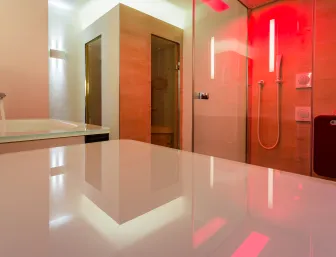 Ein modernes Badezimmer mit einer Duschkabine, die in rotes Licht getaucht ist, und einem danebenliegenden Holzsaunaraum. 