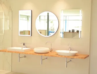 Ein modernes Badezimmer mit drei unterschiedlich geformten Waschbecken, die auf einer schwebenden Holzplatte montiert sind. 