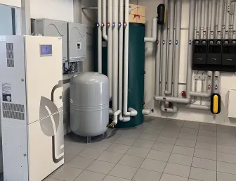 Verschiedene Komponenten einer Heiz- und Energieanlage, darunter Pufferspeicher, Regeltechnik und ein BHKW-System stehen in einem Ausstellungsraum. 
