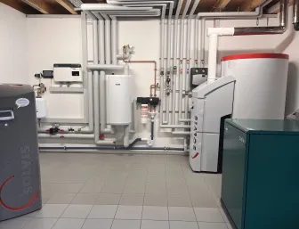 Ein Technikraum mit Fokus auf moderne Wärmeerzeugung zeigt Solvis- und Dachs-Geräte, die über ein weit verzweigtes Rohrsystem miteinander verbunden sind.