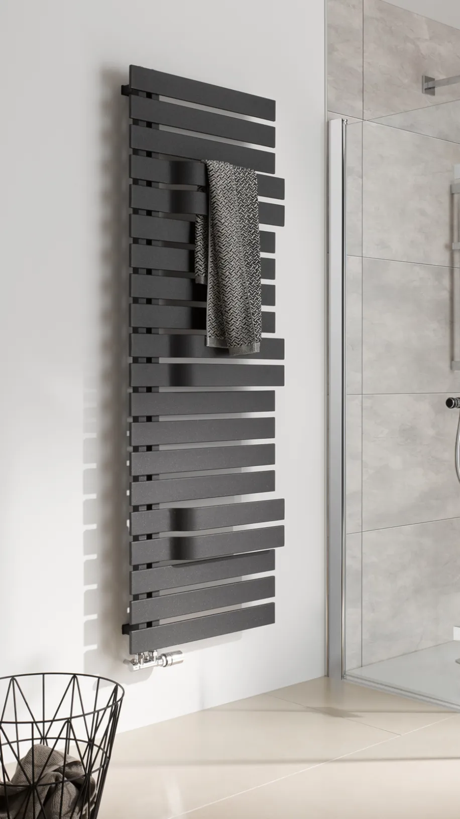Ein schwarzer HSK Yenga Handtuchheizkörper hängt an einer weißen Badezimmerwand und trägt ein graues Handtuch.