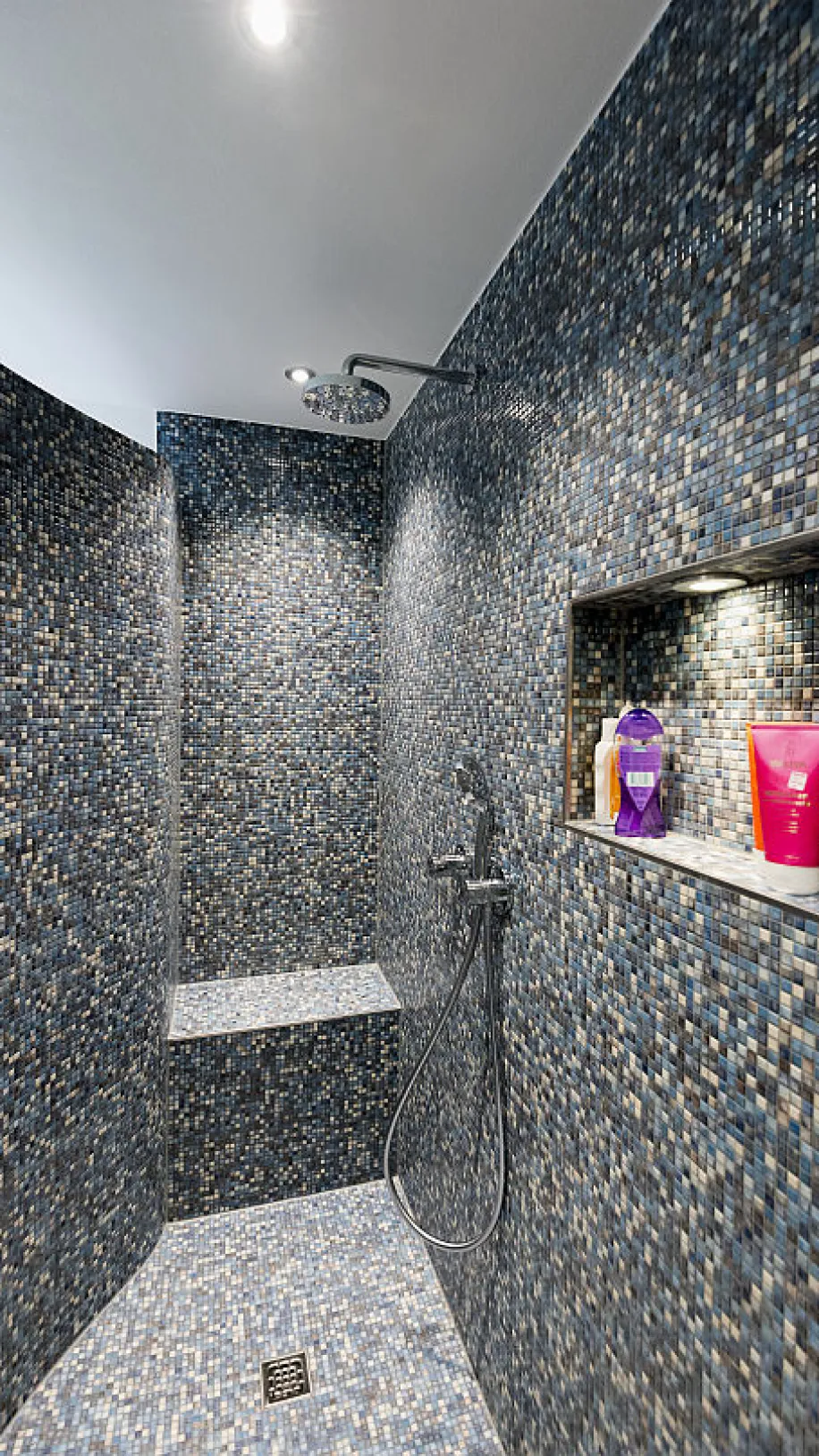 Eine Duschkabine mit glänzenden, dunkelblauen Mosaikfliesen und eingebautem Sitzbereich.