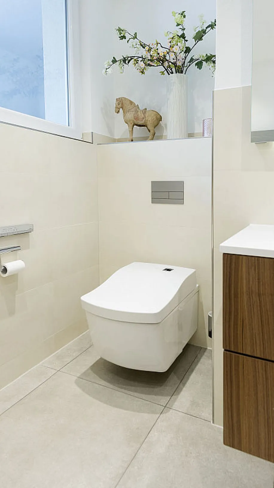 Badezimmer mit wandhängendem TOTO Dusch-WC, cremefarbenen Fliesen und einem kleinen Fenster.