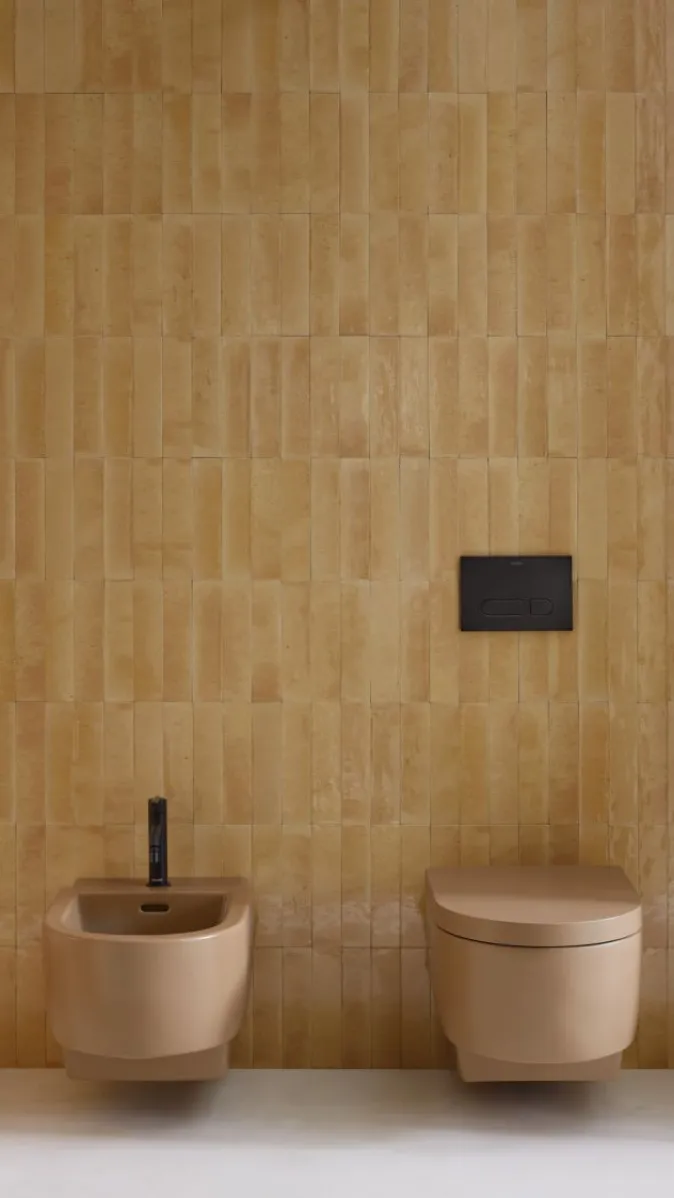 WC und Bidet der Serie Balcoon von Duravit in Schwarz vor einer goldbraun gefliesten Wand.