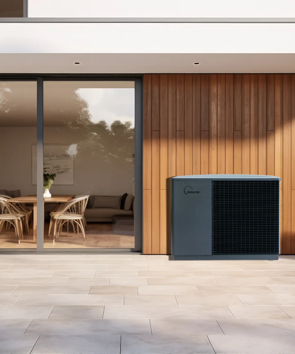 Eine Solvis-Wärmepumpe steht auf einer großzügigen Terrasse vor einer modernen Hausfassade mit Holz- und Glasflächen.