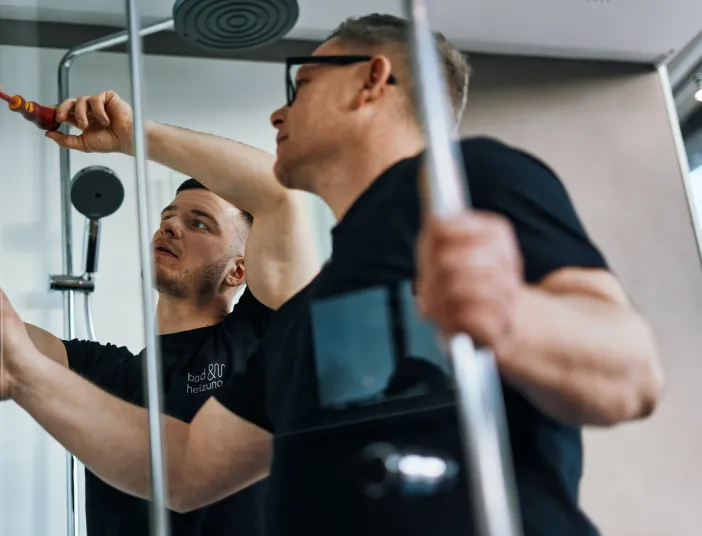 Anlagenmechaniker SHK montieren eine Duschtür.