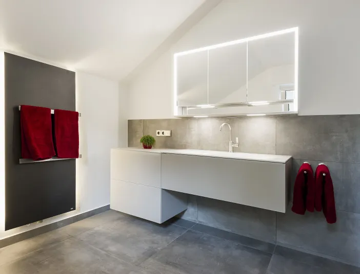 Heller Waschplatz mit weißen Unterschrank neben schwarzem Designheizkörper von Bemm.