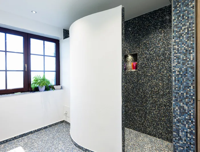 Badezimmer mit geschwungener Dusch-Trennwand und blauen Mosaikfliesen.